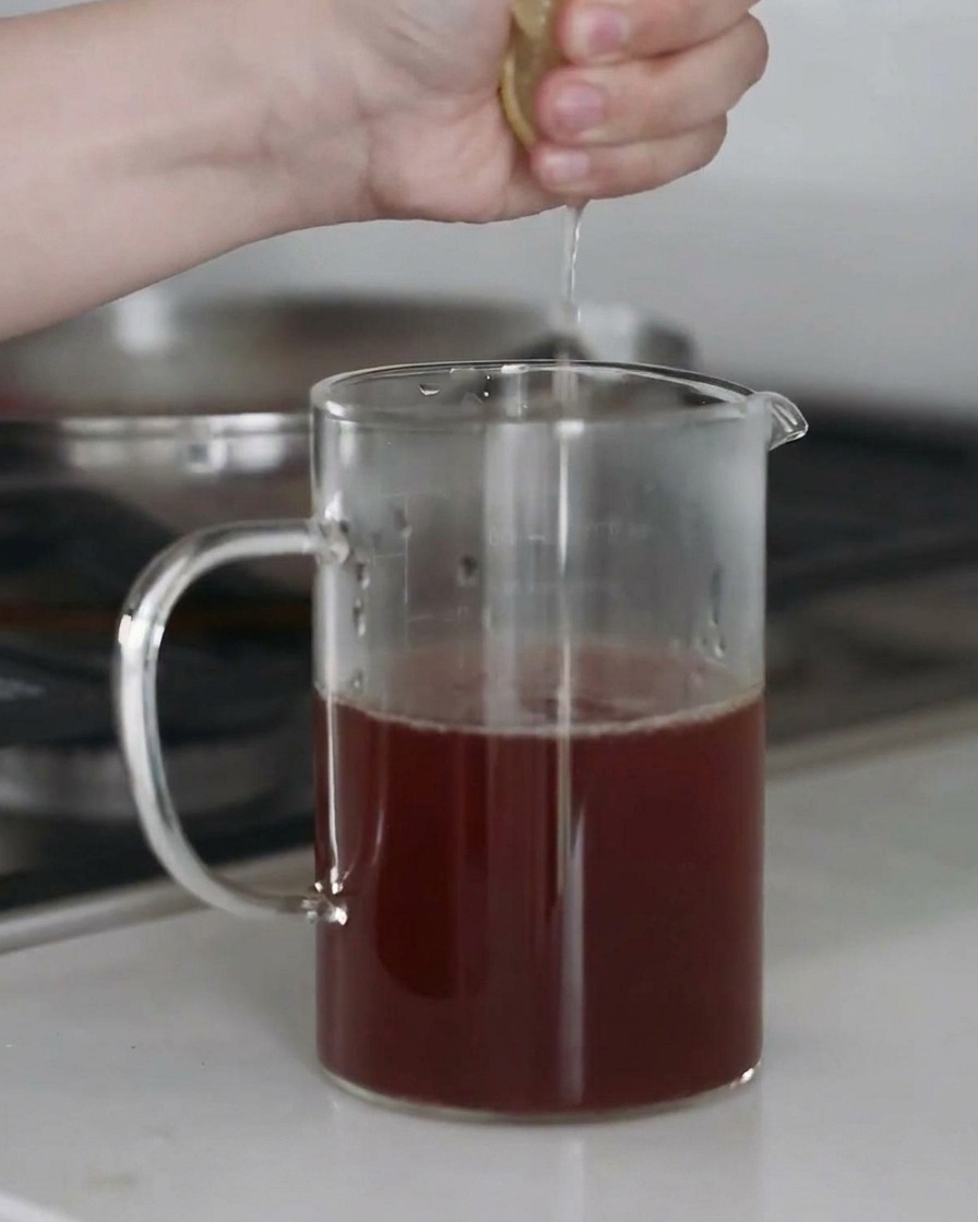 Succo di limone fresco spremuto in una ciotola di brodo, con goccioline catturate a mezzaria.