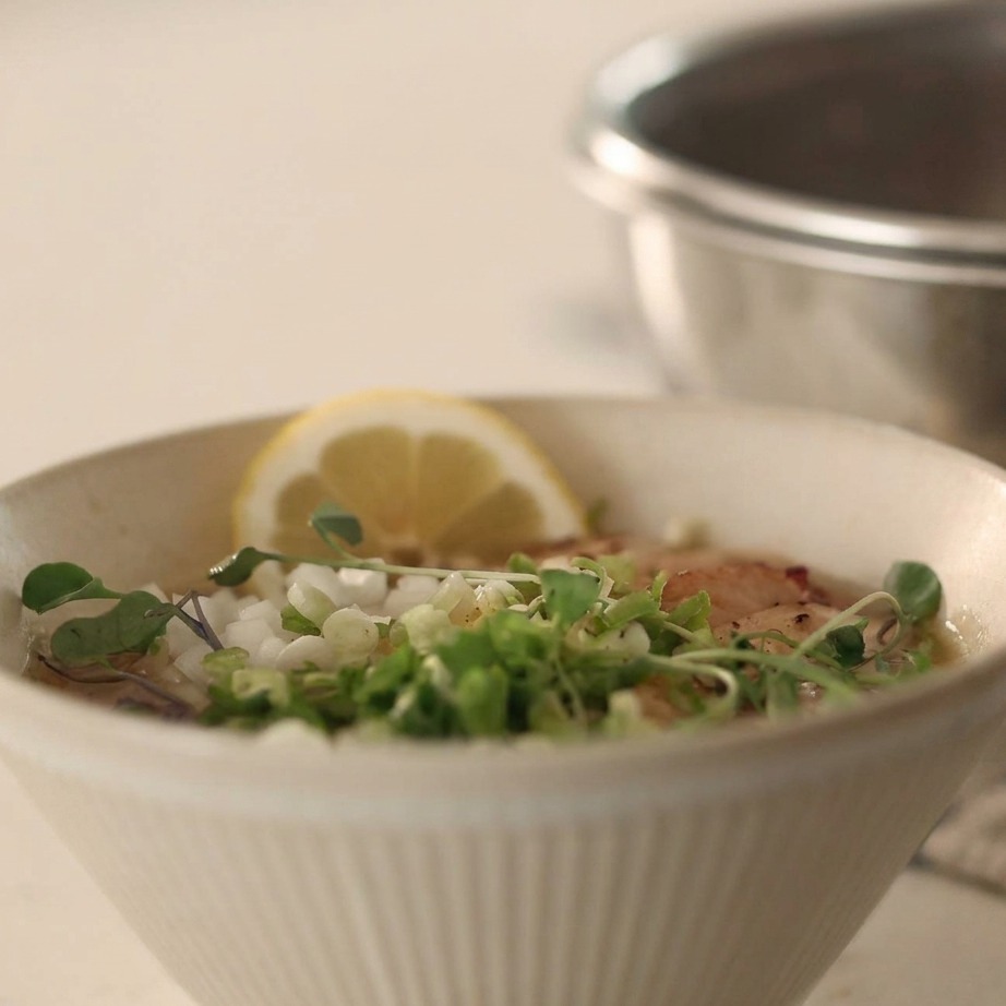 Una ciotola di noodles freddi nel brodo guarnita con cipolla tritata, cipollotto e pepe nero.