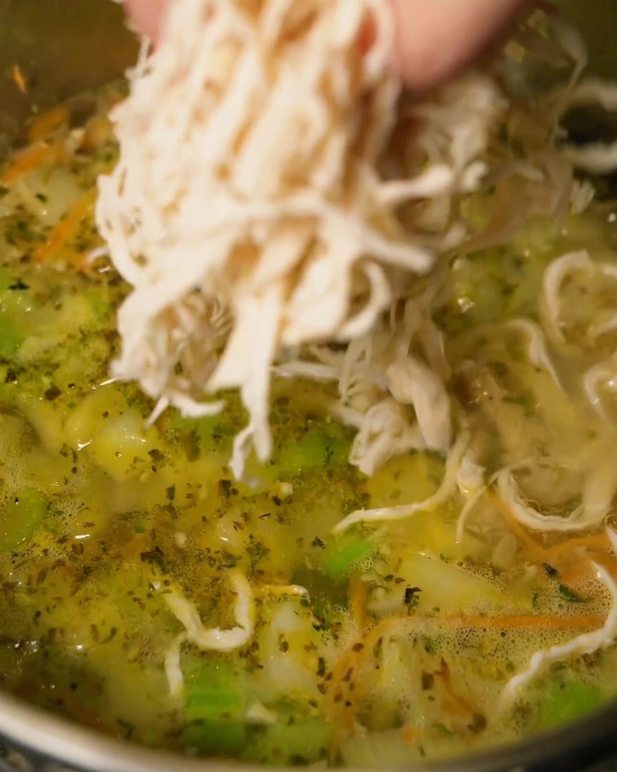 Pollo sfilacciato aggiunto a una pentola di zuppa in ebollizione.
