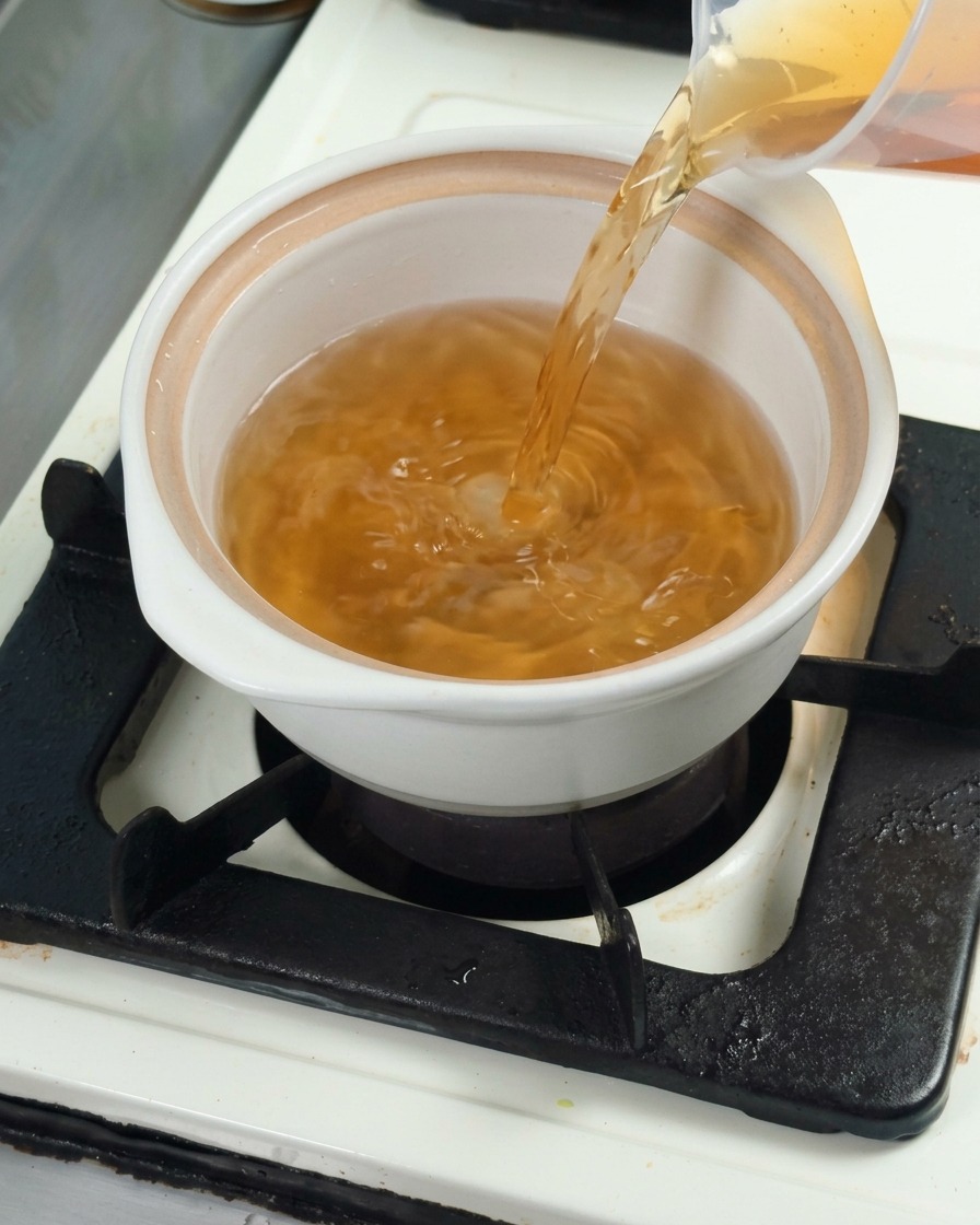 Brodo di kombu dashi versato in una pentola di ceramica bianca, preparando la base per la cottura.