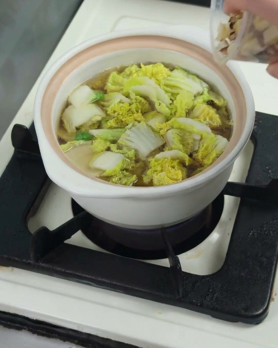 Pezzi di coscia di pollo cruda aggiunti in una pentola contenente baby bok choy ammorbidito nel brodo.