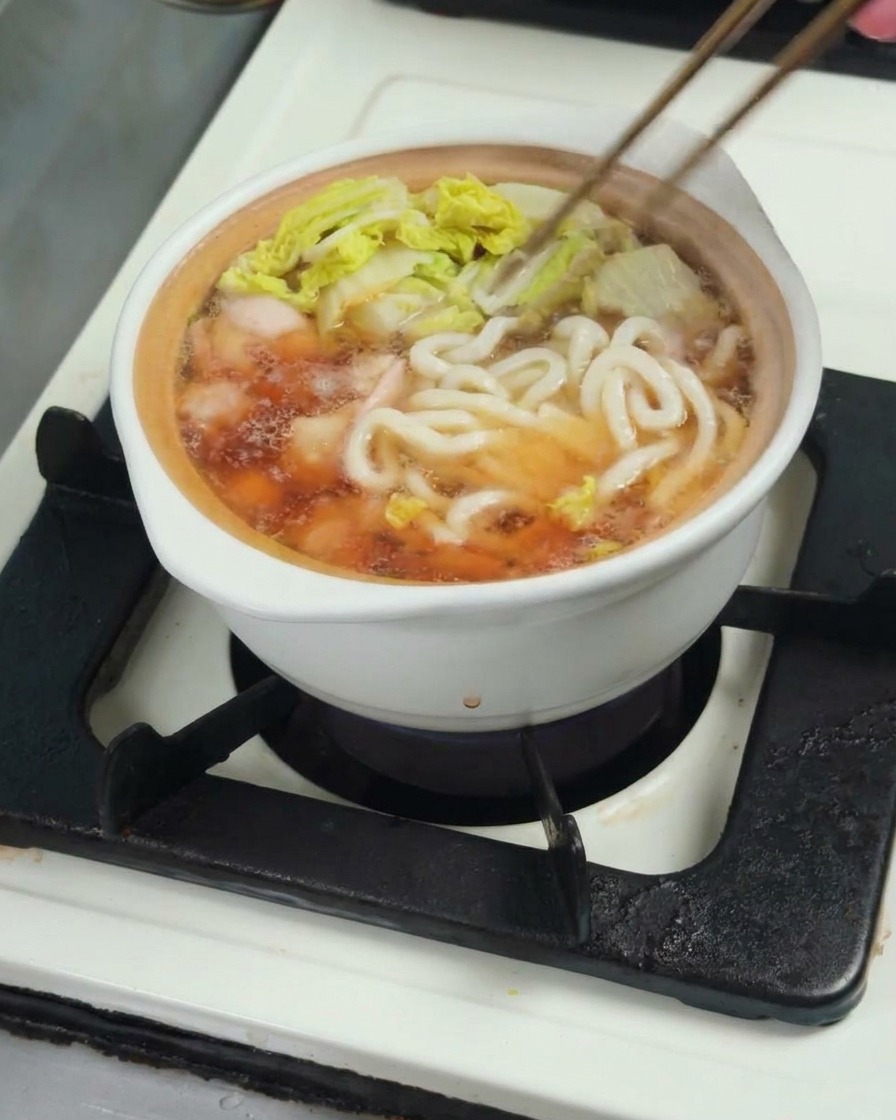Noodles udon aggiunti nella pentola di brodo, pollo e bok choy per terminare la cottura.