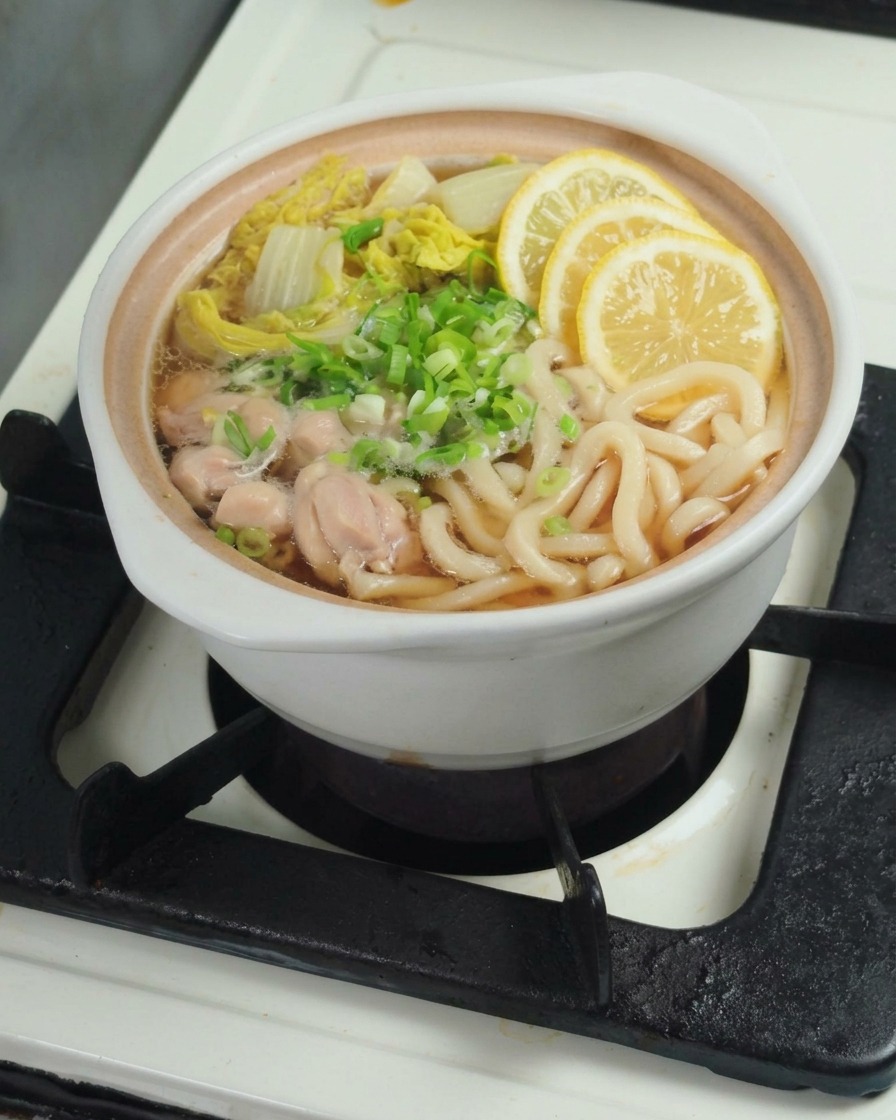 Mano che spreme uno spicchio di limone fresco in una pentola contenente udon e bok choy.