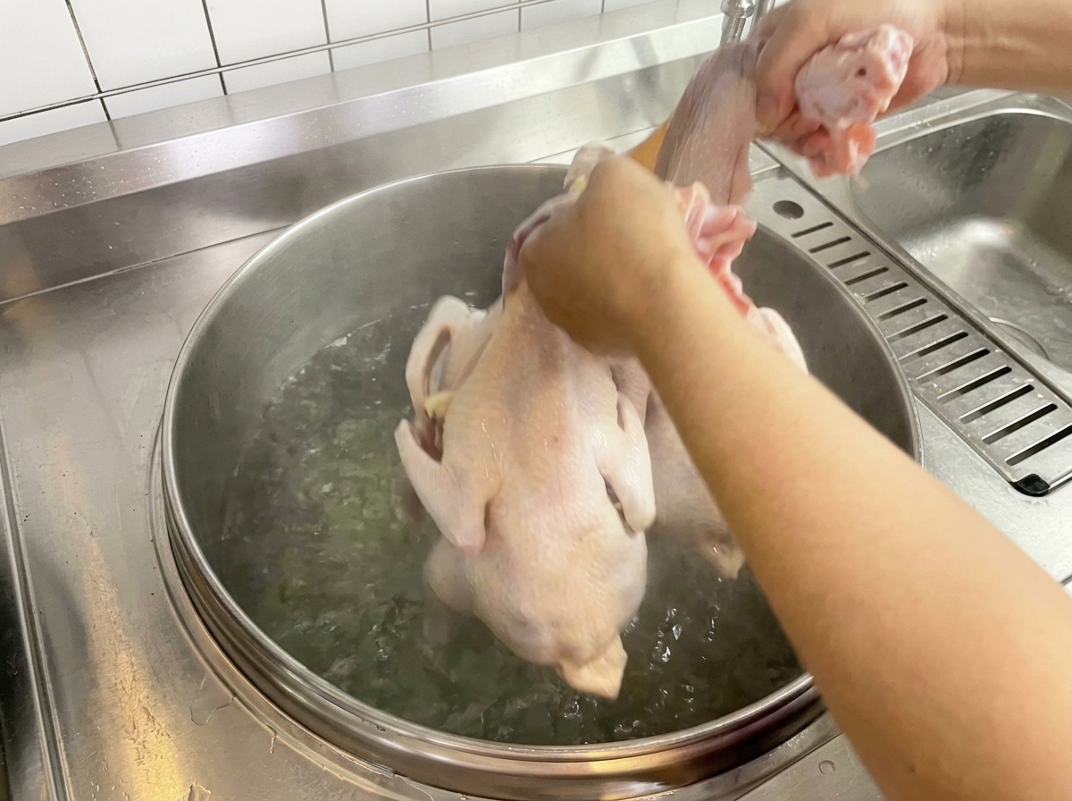 Un pollo crudo immerso a mano in una pentola capiente di acqua bollente.