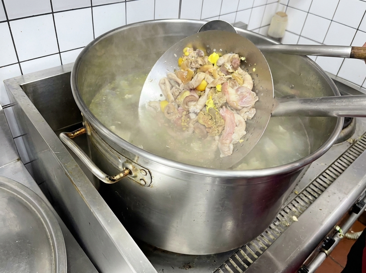Interiora di pollo sbollentate in un colino metallico sopra lacqua bollente.