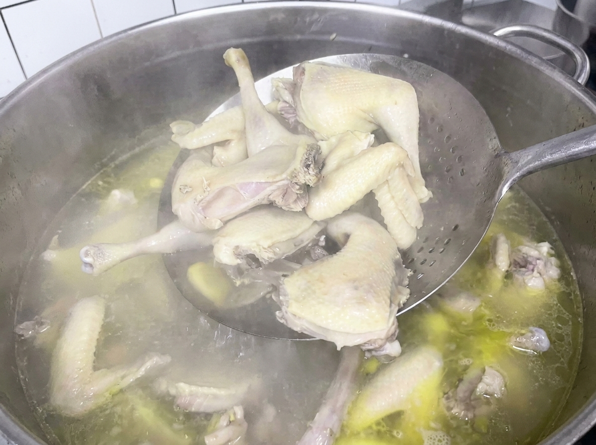 Pezzi di pollo bolliti prelevati dalla pentola con una schiumarola a ragno.