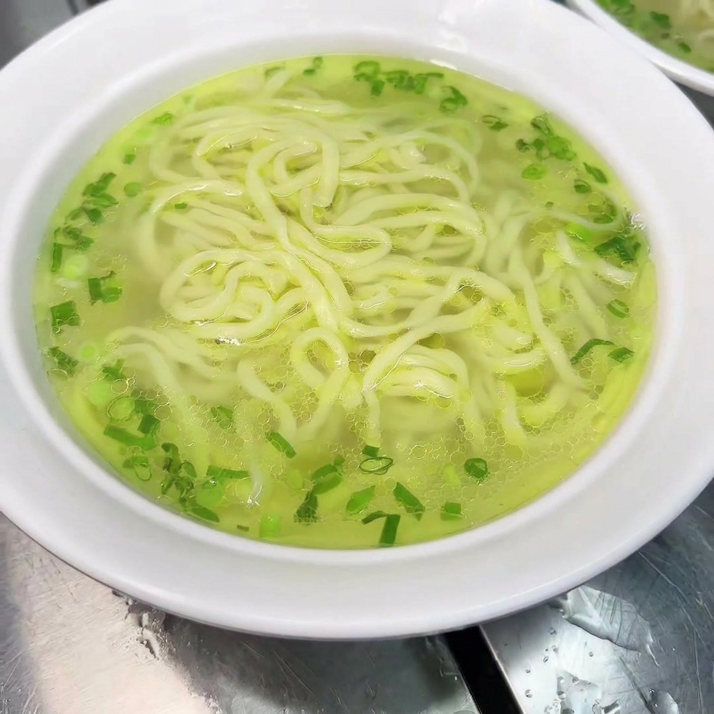 Una ciotola di tagliolini guarnita con una coscia di pollo cotta e brodo caldo.