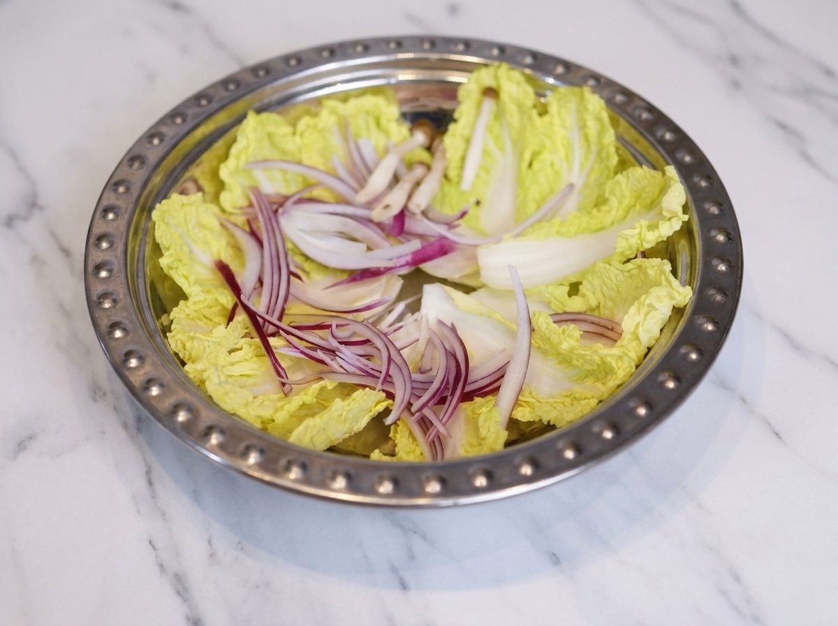 Unampia pentola di metallo con cavolo, cipolle, funghi, tortini di pesce e fette di carne in scatola disposti con ordine.