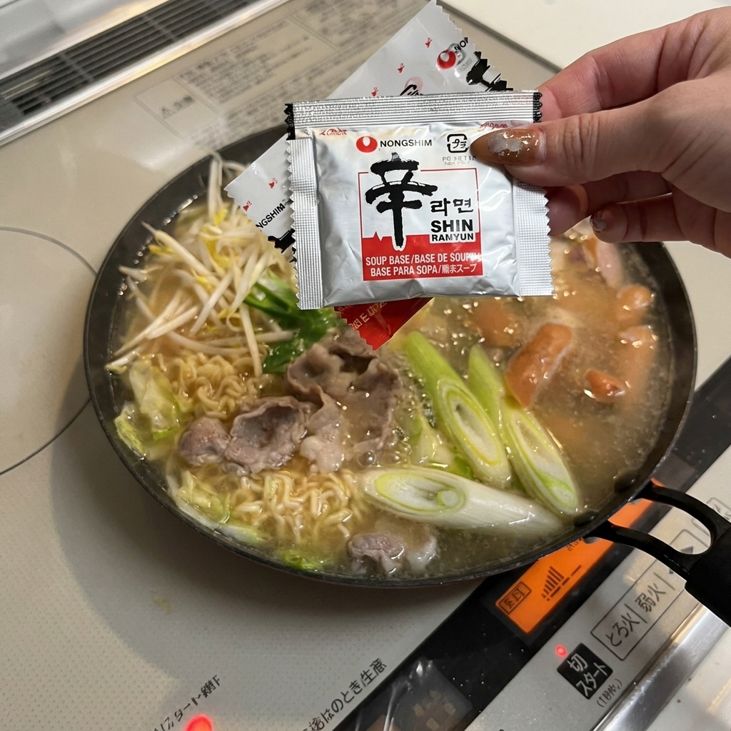 Una mano che versa la bustina di condimento dei noodles nel brodo.