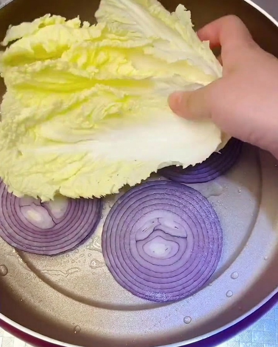 Foglie di cavolo Napa fresco posizionate nella padella sopra lo strato di cipolle.