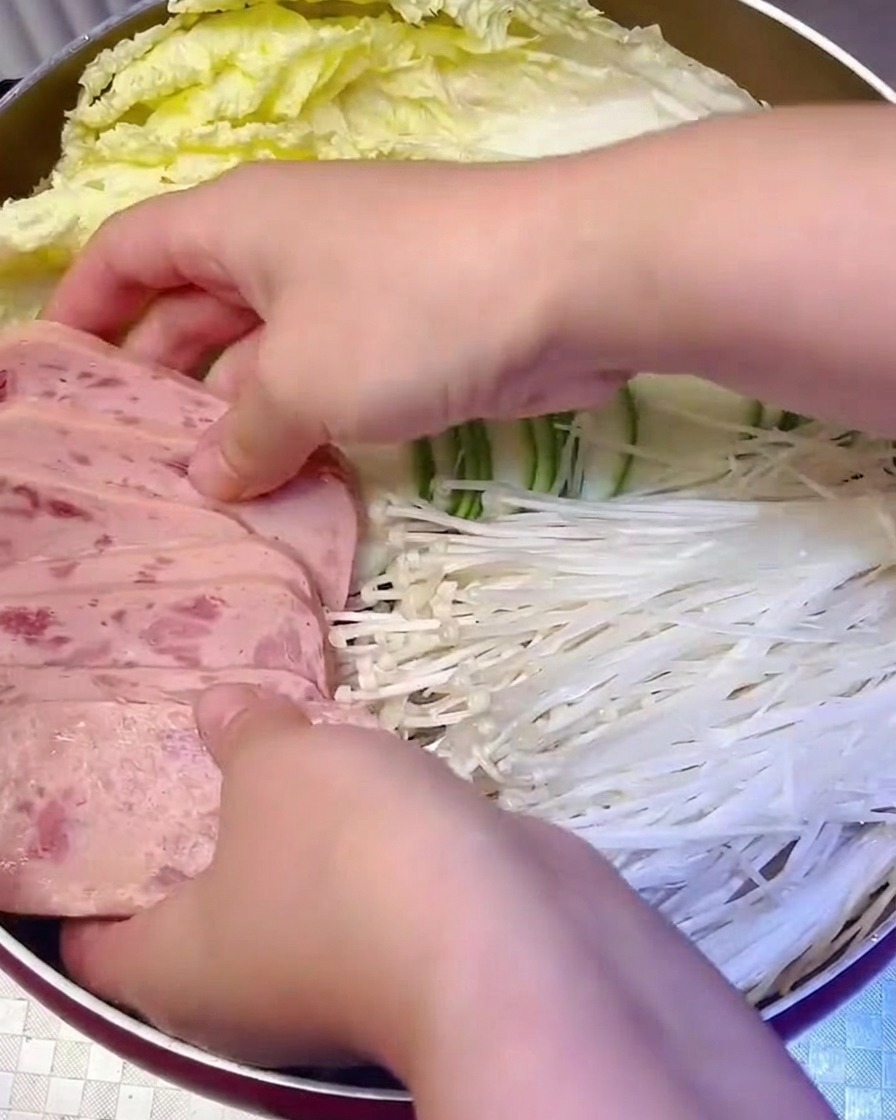 Carne in scatola a fette e funghi enoki disposti sistematicamente nella pentola.