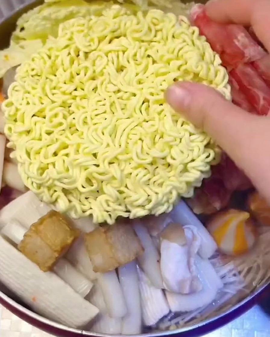 Blocco di noodles istantanei coperto da fette di formaggio giallo nella pentola.