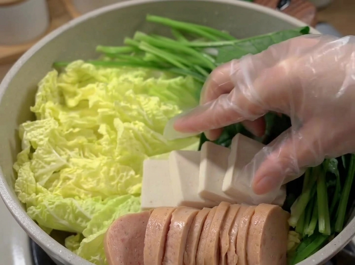 Una pentola ampia riempita con strati disposti con cura di carne, tofu, torte di pesce e verdure.