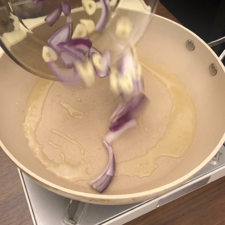Vongole fresche, cipolle tritate e aglio vengono versati in una padella con olio caldo.