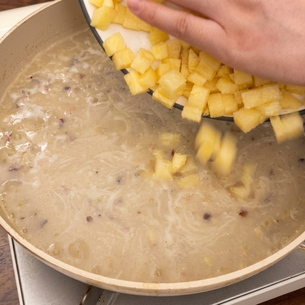 Mano che lascia cadere cubetti di patate nella padella con la zuppa che sobbolle.