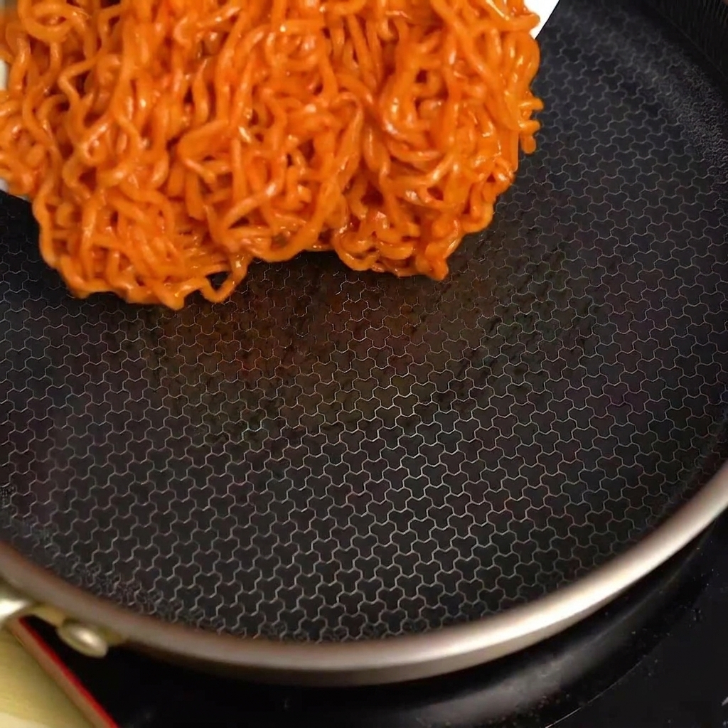 Noodles piccanti versati da una ciotola in una padella nera calda e vuota.