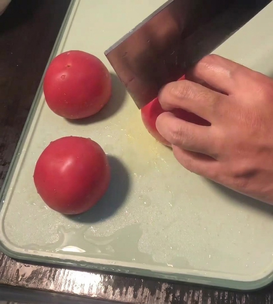 Primo piano di una mano che usa un coltello per incidere una croce sulla buccia di un pomodoro fresco.