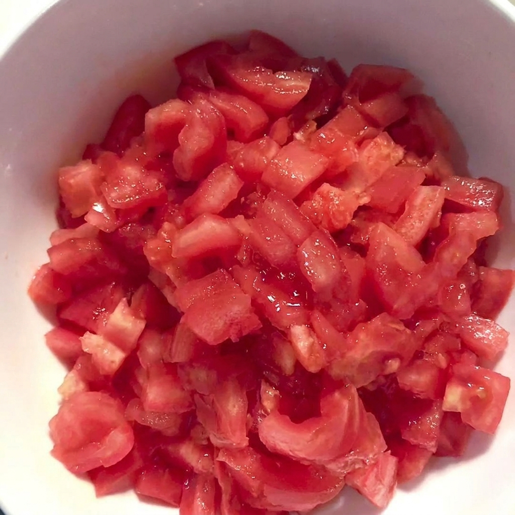 Una ciotola bianca piena di pomodori pelati e tagliati a cubetti.