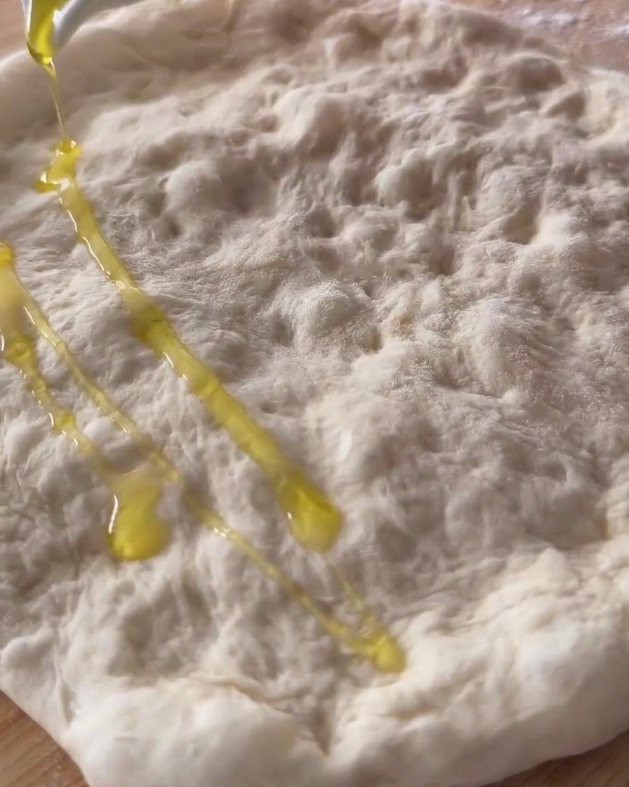 Olio doliva versato sullimpasto della pizza crudo, steso e bucherellato.