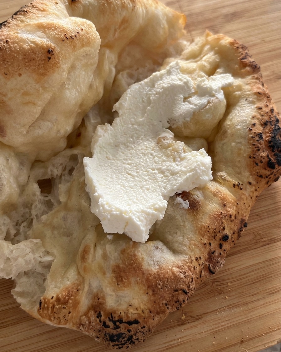 Un generoso strato di ricotta bianca spalmato allinterno di un pane pizza appena sfornato.