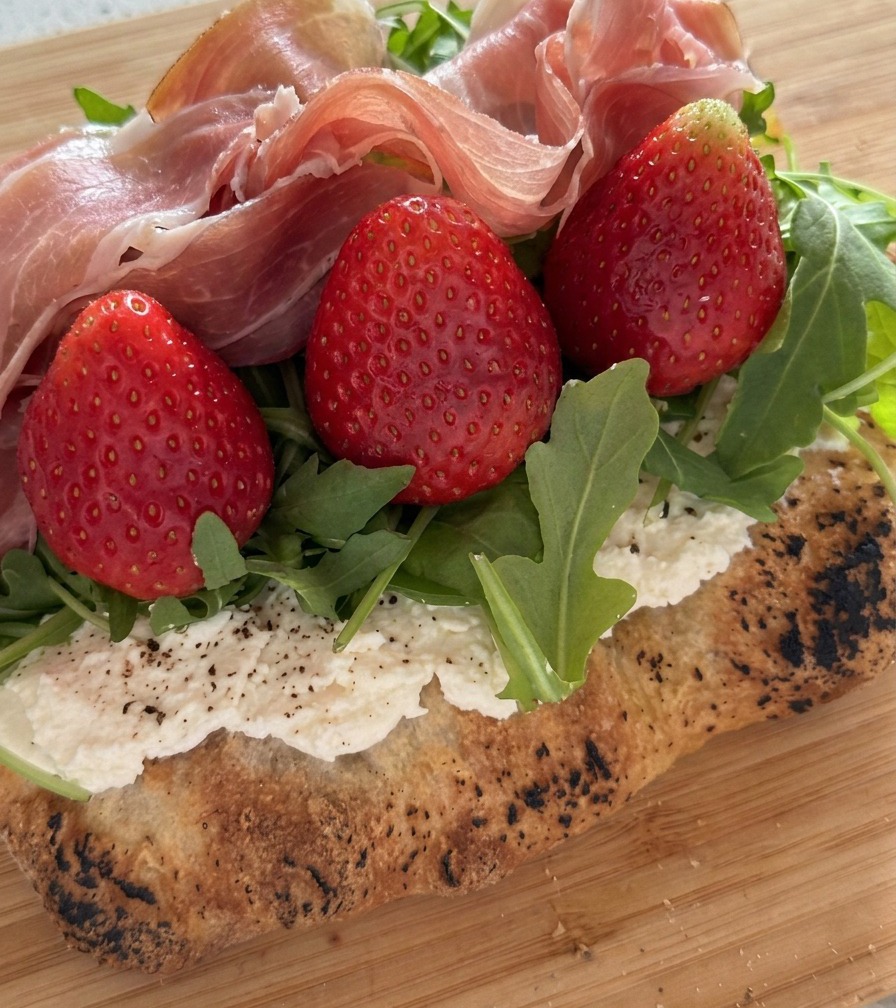 Un primo piano di fette di prosciutto crudo piegate e stratificate su fragole fresche e rucola.