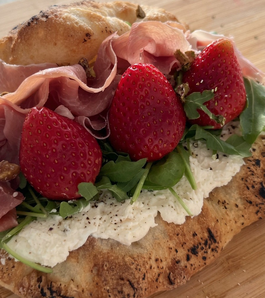 Pistacchi tritati spolverati su un panino ripieno di prosciutto, fragole e rucola.