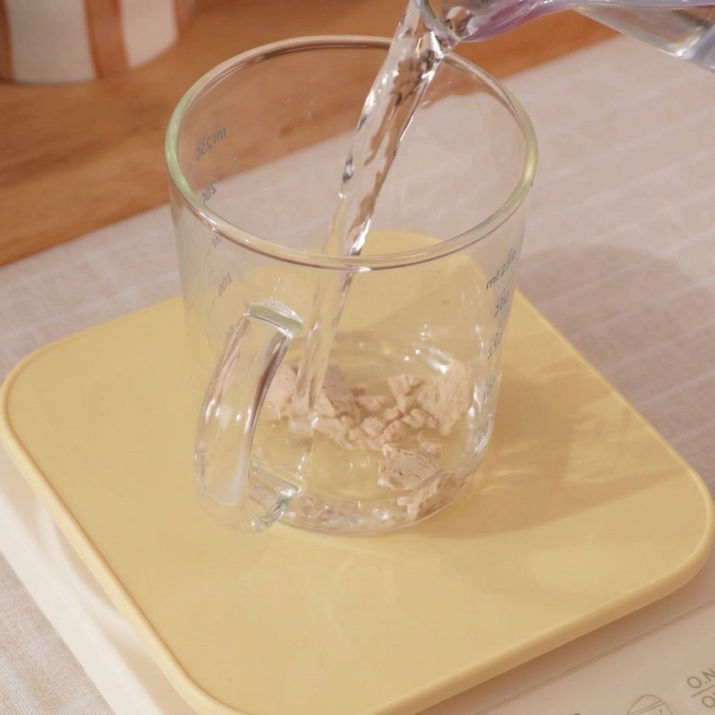 Primo piano di un misurino con acqua ghiacciata e lievito mescolati con una piccola frusta.