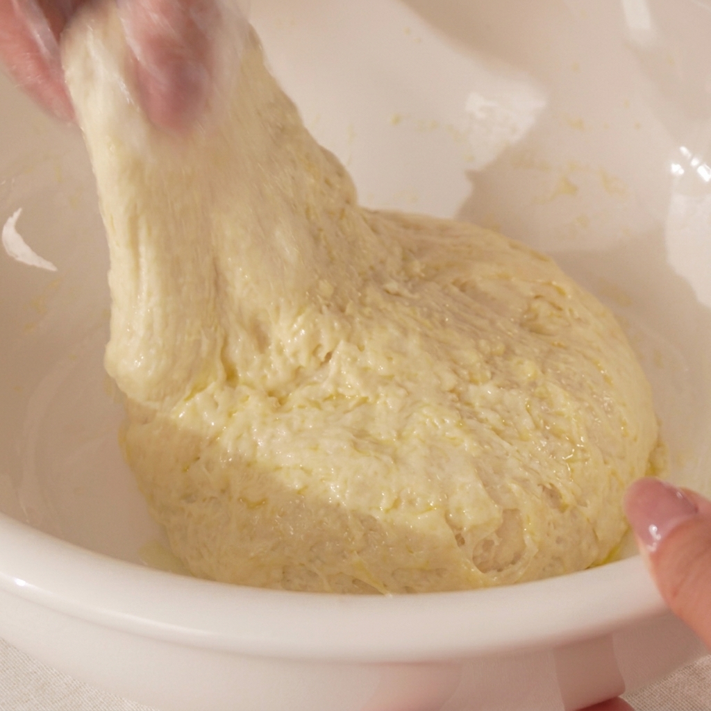 Primo piano di mani che tirano e ripiegano limpasto della pizza su se stesso.