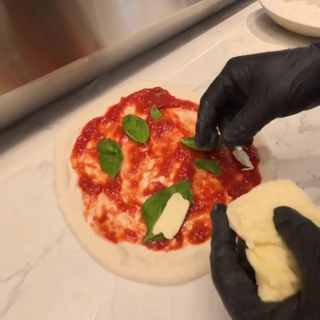 Pezzi di mozzarella fresca adagiati sopra uno strato di rucola su impasto crudo.