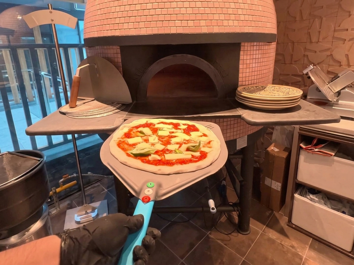 Una pizza su una pala di metallo pronta per essere infornata in un forno a legna tradizionale.