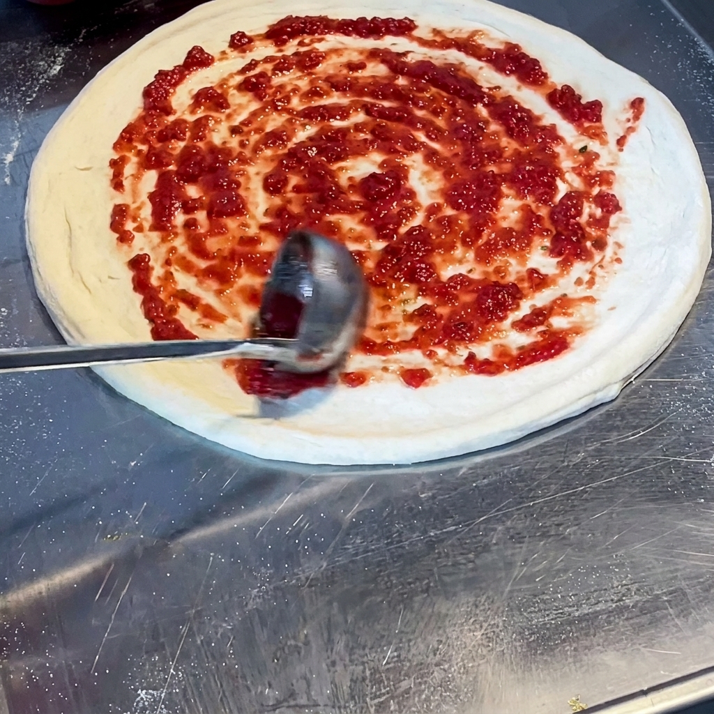 Un mestolo che stende la salsa di pomodoro rossa con un movimento a spirale sulla base.