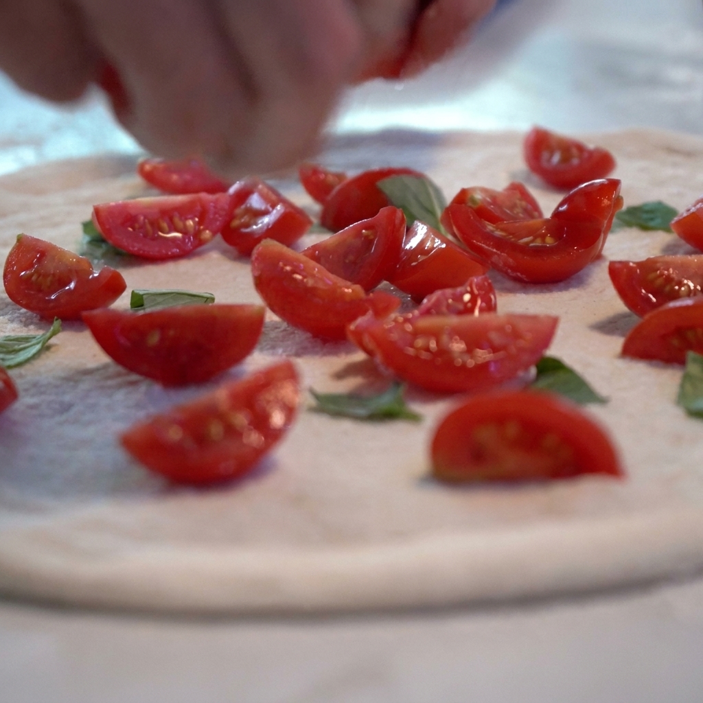 Salsa di pomodoro e fette di pomodoro fresco aggiunte sul disco di pasta della pizza cruda.