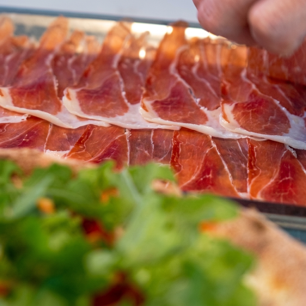Fette sottili di prosciutto disposte accuratamente sopra la pizza ricoperta di rucola.