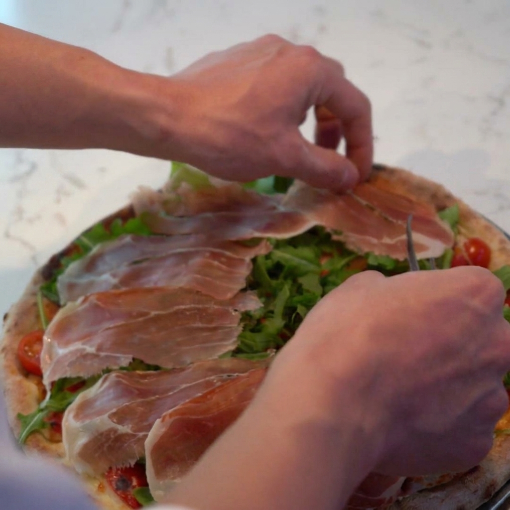 Parmigiano grattugiato spolverato sulla pizza, a ricoprire prosciutto e rucola.