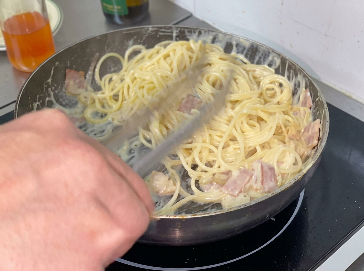 Spaghetti cotti aggiunti alla salsa cremosa in padella.