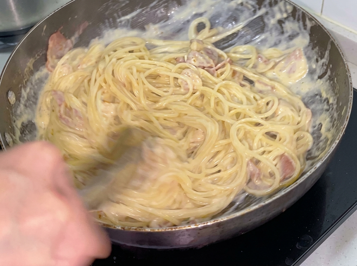 Spaghetti cremosi mescolati con pollo e pancetta in padella.