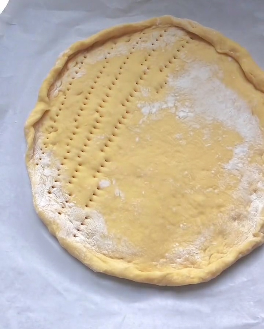 Una base pizza cruda su carta forno con piccoli fori praticati uniformemente.