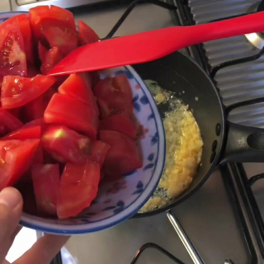 Pezzetti di pomodoro aggiunti in una pentola nera con burro fuso e aglio.
