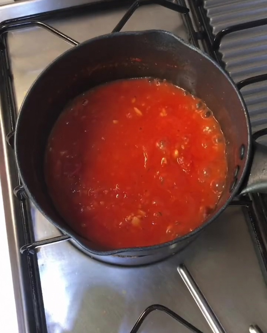 Sugo di pomodoro denso e borbottante in una pentola nera sul fornello.