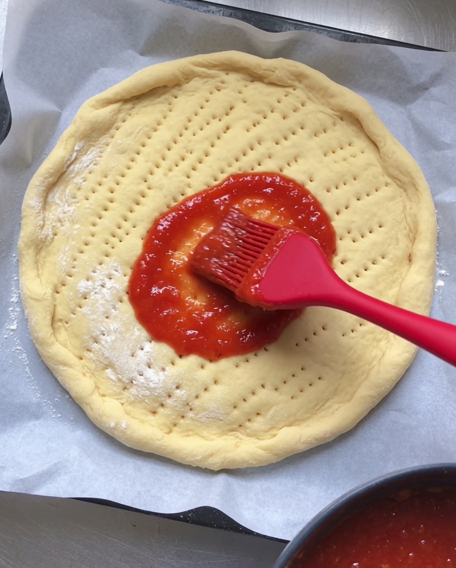 Sugo di pomodoro steso uniformemente su una base pizza cruda.