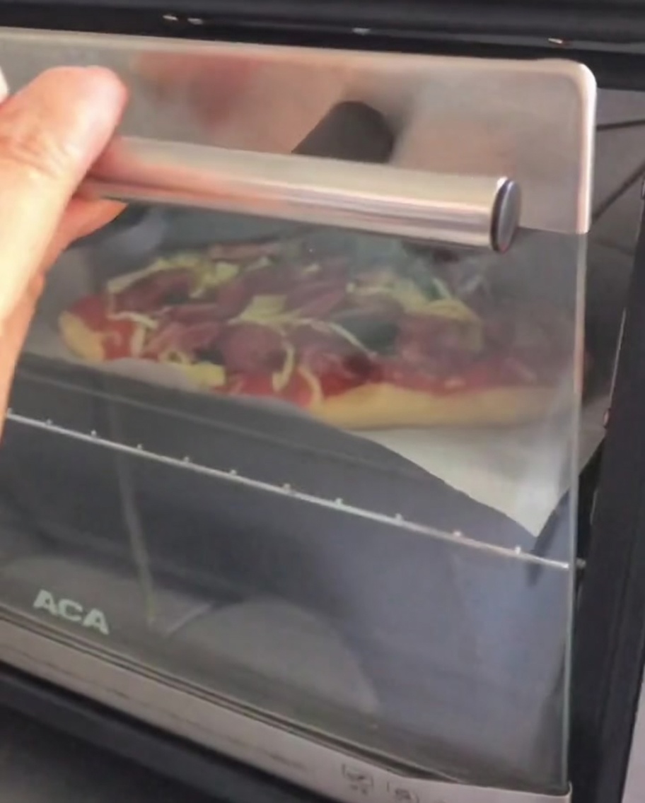 Porta di un forno aperto mentre una teglia con la pizza viene inserita.