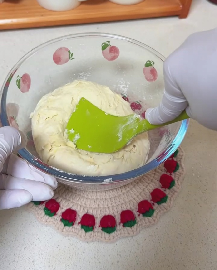 Mani con guanti che usano una spatola in silicone per mescolare un impasto grezzo in una ciotola.