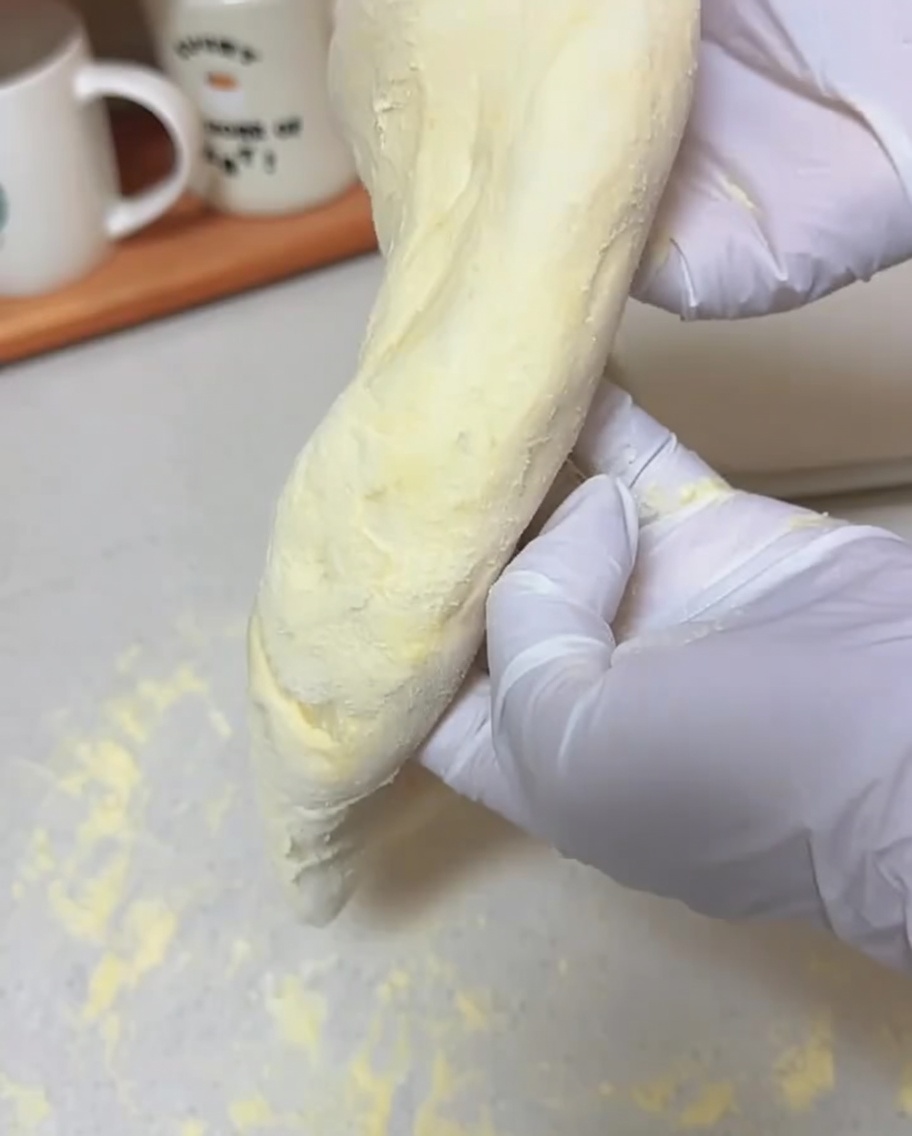 Mani che tengono un pezzo di impasto, lasciando che la gravità lo stenda.