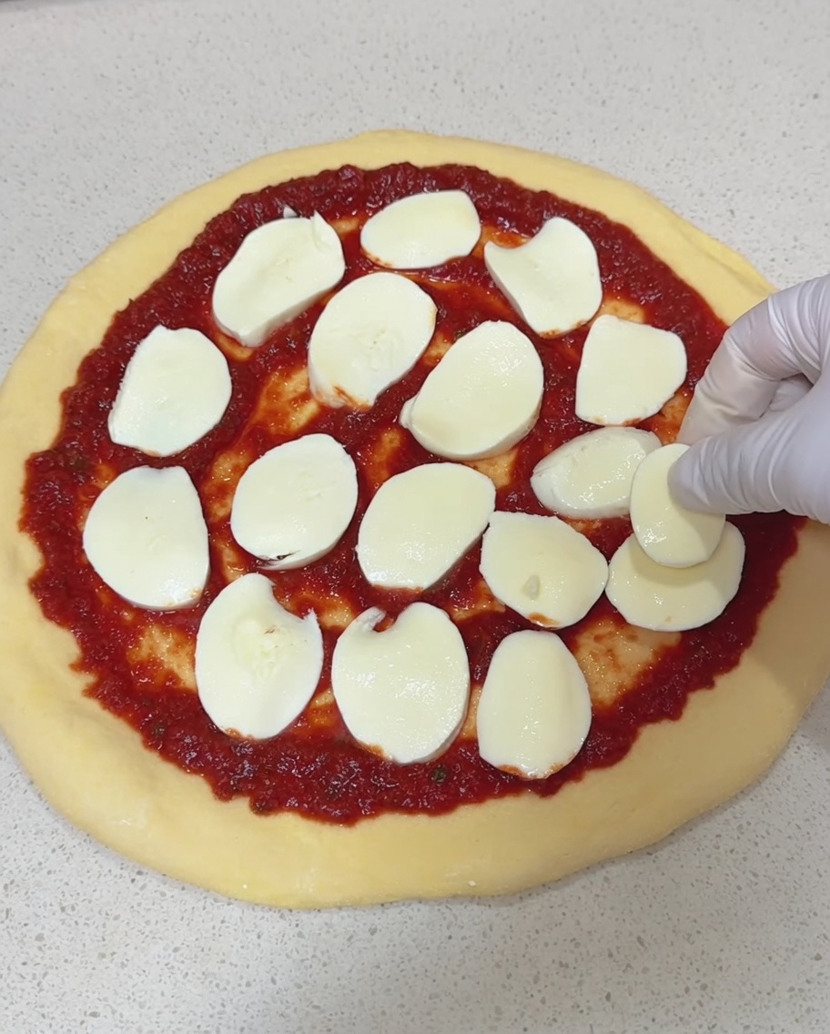 Posizionamento di fette di mozzarella fresca sulla base condita.