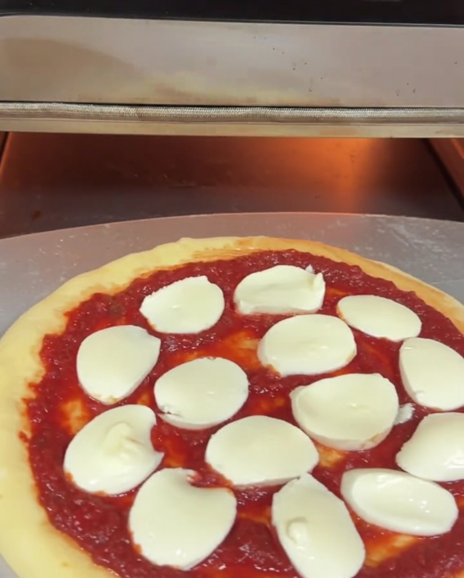 Pizza cruda inserita nel forno elettrico tramite una pala metallica.