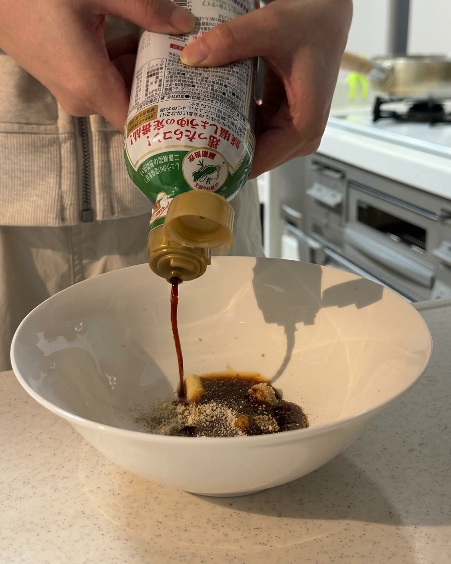 Mani che versano salsa di soia a basso contenuto di sodio da una bottiglia in una ciotola bianca contenente spezie secche e pasta.