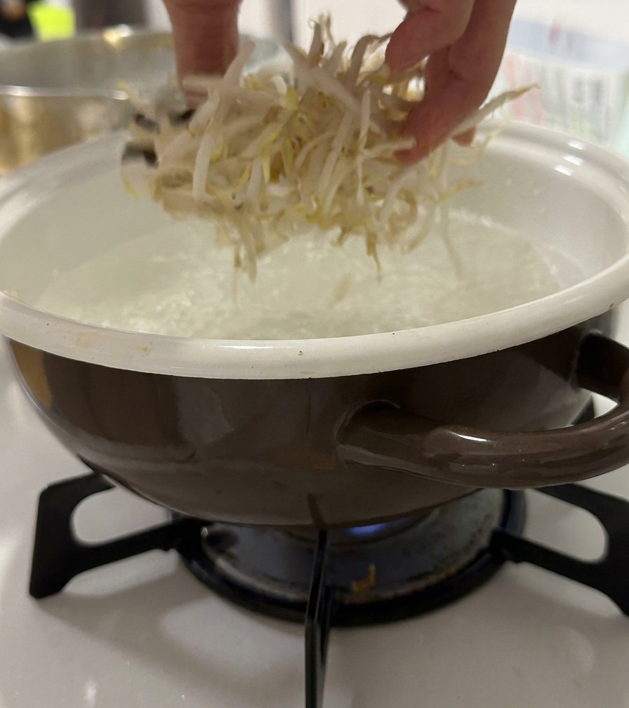 Una mano che getta germogli di soia freschi in una pentola di acqua bollente.