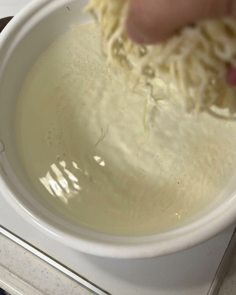 Una mano che getta una porzione di noodles ramen freschi in una pentola di acqua in rapida ebollizione.