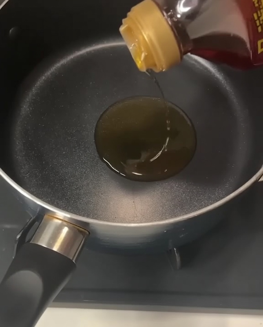Una bottiglia versa olio di sesamo dorato in una pentola nera vuota sui fornelli.