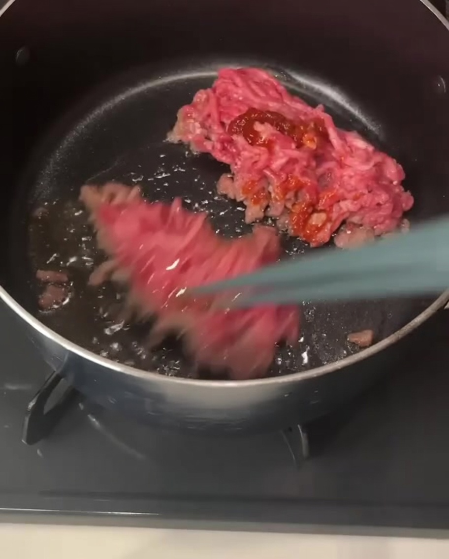 Bacchette che sollevano e mescolano pezzi di carne di maiale macinata ricoperti di pasta di peperoncino rossastra in una pentola.